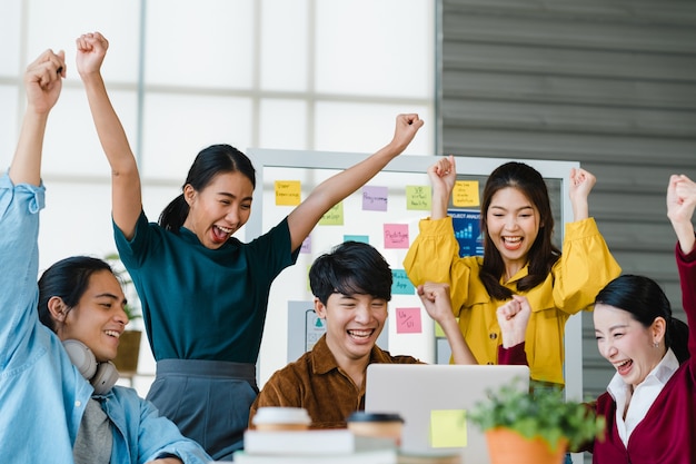 Gruppe asiatischer junger kreativer Leute in der intelligenten Freizeitkleidung, die das Geschäft bespricht, feiern das Geben von fünf, nachdem sie sich glücklich gefühlt und einen Vertrag oder eine Vereinbarung im Amt unterzeichnet haben. Teamwork-Konzept für Mitarbeiter.