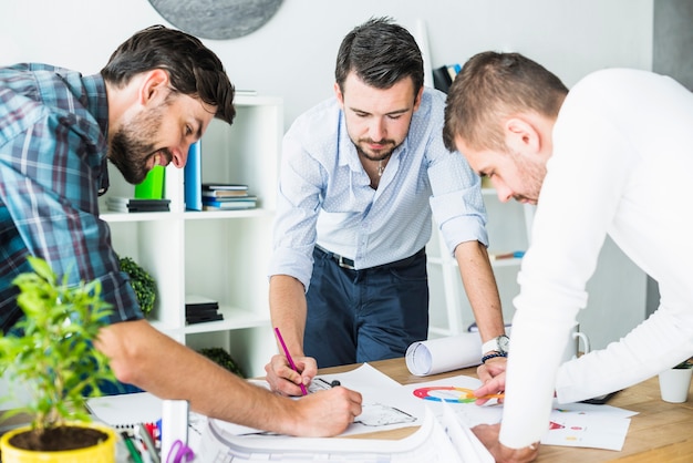 Gruppe des männlichen Architekten, der Plan über hölzernem Schreibtisch plant