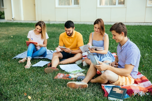 Gruppe des Studierens von den Kursteilnehmern, die auf Gras mit Anmerkungsbüchern sitzen