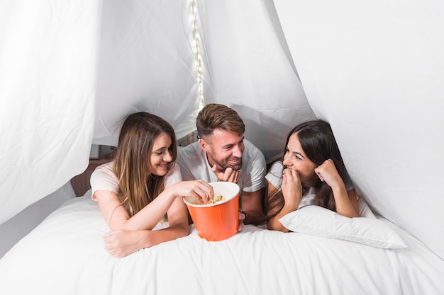 Gruppe Freunde, die auf dem Bett isst Popcorn liegen