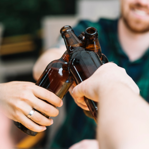 Gruppe Freunde, welche die braunen Bierflaschen klirren