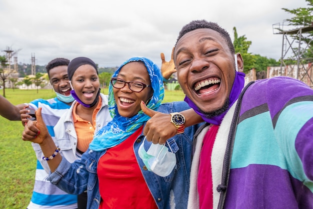 Gruppe fröhlicher afrikanischer Freunde mit Gesichtsmasken, die ein Selfie in einem Park machen