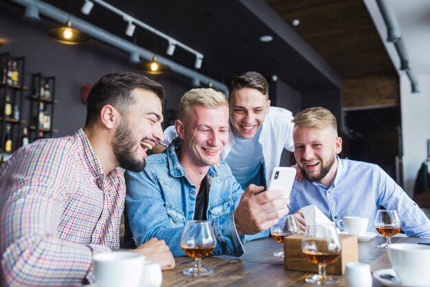Gruppe glückliche Freunde, die den Smartphone sitzt am Restaurant betrachten