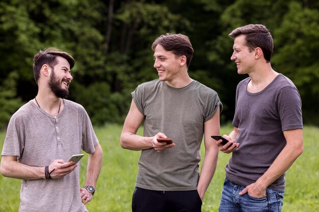 Gruppe glückliche Kerle mit Smartphones plaudernd in der Natur