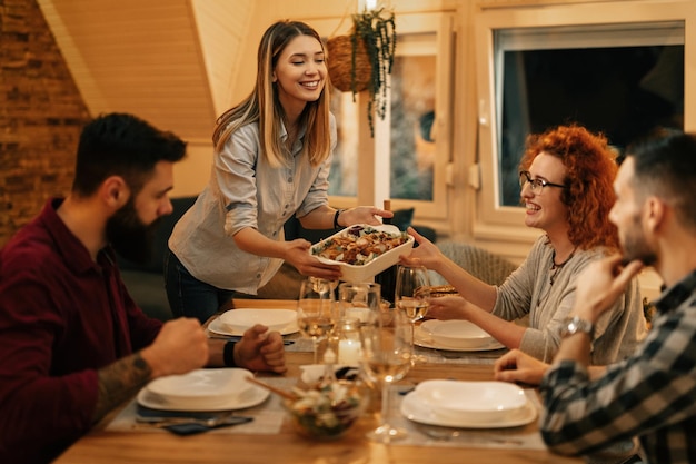 Gruppe glücklicher Freunde, die im Speisesaal zu Abend essen Der Fokus liegt auf der Frau, die Essen am Tisch serviert