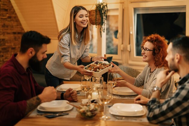 Gruppe glücklicher Freunde, die im Speisesaal zu Abend essen Der Fokus liegt auf der Frau, die Essen am Tisch serviert