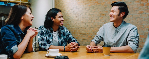 Kostenloses Foto gruppe glücklicher junger asiatischer freunde, die spaß haben und lachen, während sie zusammen im café-restaurant sitzen.