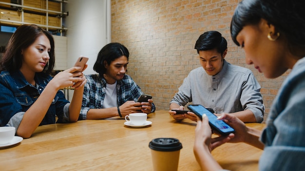 Gruppe glücklicher junger asiatischer Freunde, die Spaß haben und zusammen Smartphone verwenden, während sie zusammen im Café-Restaurant sitzen