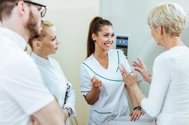 Gruppe glücklicher Mitarbeiter des Gesundheitswesens, die vor dem MRT-Scan-Verfahren im Krankenhaus mit einem reifen Patienten sprechen. Der Fokus liegt auf der glücklichen Krankenschwester