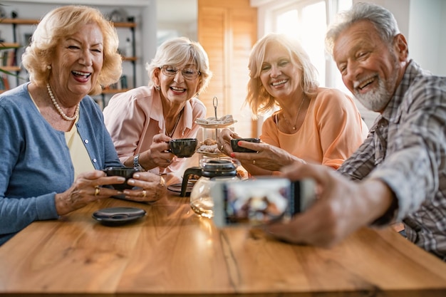 Gruppe glücklicher reifer Freunde, die Spaß haben, während sie sich zu Hause versammeln und Selfies mit dem Smartphone machen