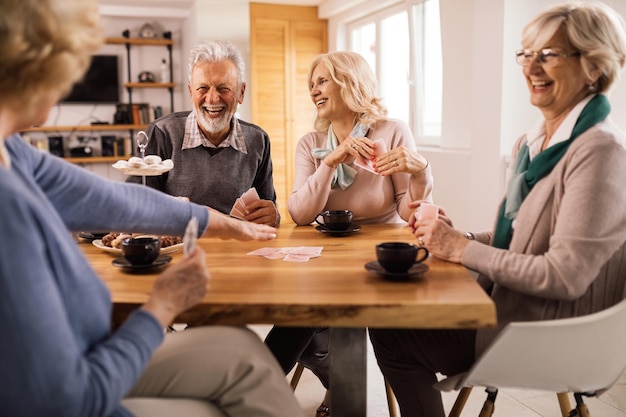 Gruppe glücklicher, reifer Menschen, die beim Kartenspiel am Tisch lachen