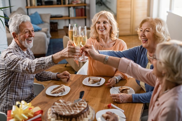 Gruppe glücklicher Senioren, die mit Champagner anstoßen und Spaß haben, während sie zu Hause Geburtstag feiern