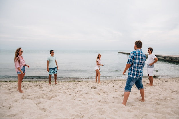 Gruppe junge attraktive Freunde, die Frisbee auf dem Strand, durch das Meer spielen