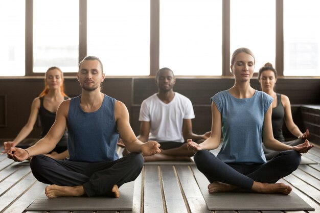 Gruppe junge sportliche Leute, die in Sukhasana sitzen, trainieren