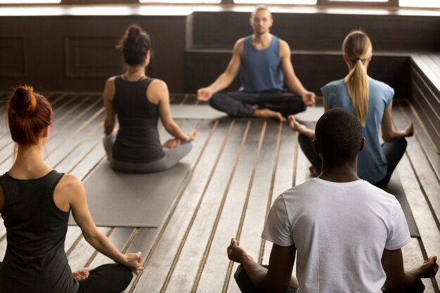 Gruppe junge sportliche Leute, die in Sukhasana sitzen, trainieren