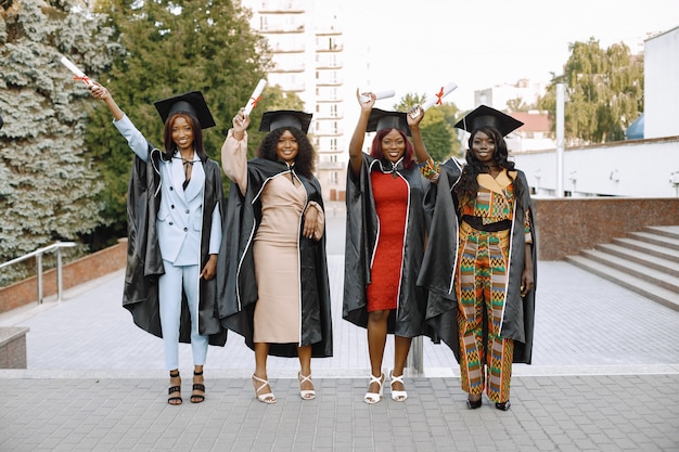 Gruppe junger afroamerikanischer studentinnen in schwarzem abschlusskleid. campus als hintergrund