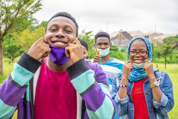 Gruppe junger fröhlicher afrikanischer Freunde mit Gesichtsmasken und sozialer Distanzierung in einem Park