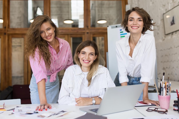 Gruppe junger, fröhlicher Frauen mit Laptop, die glücklich in die Kamera schauen