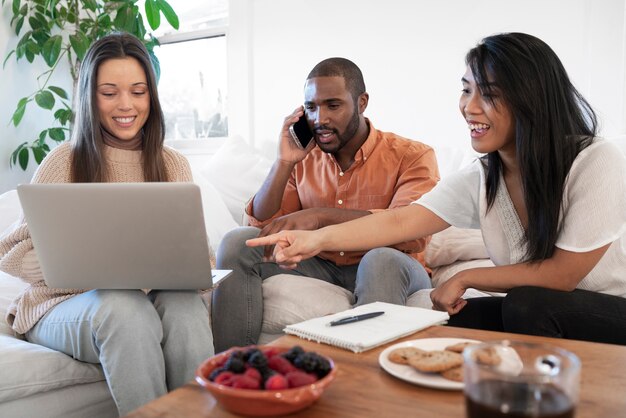 Gruppe junger Leute, die zu Hause zusammen Laptop auf dem Sofa benutzen und Snacks essen