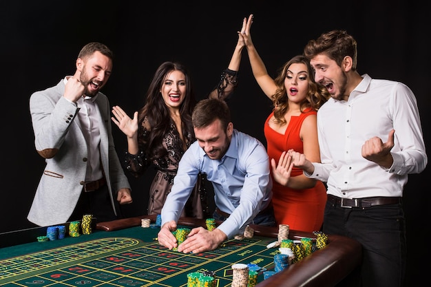 Kostenloses Foto gruppe junger leute hinter roulette-tisch auf schwarzem hintergrund. gewinnender spieler. helle emotionen