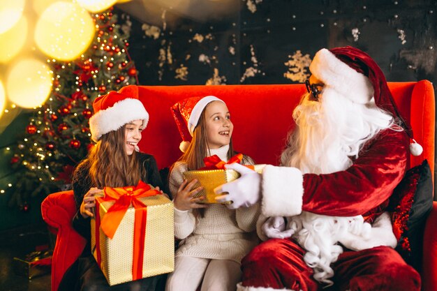 Gruppe Kinder, die mit Sankt und Geschenken auf Weihnachtsabend sitzen