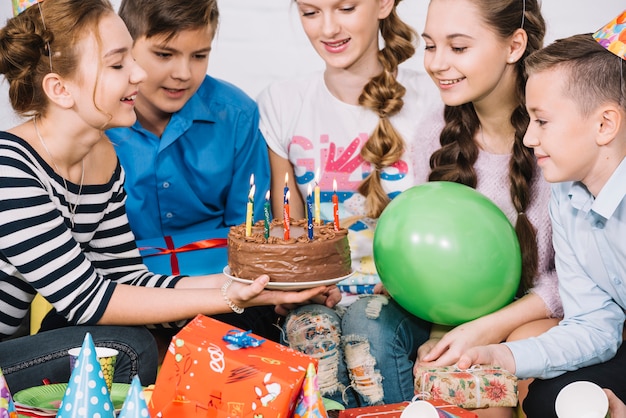 Gruppe lächelnde Freunde, die Geburtstagskuchen mit belichteten Kerzen betrachten