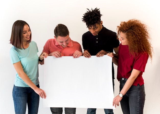 Gruppe lächelnde multiethnische Freunde, die das leere weiße Plakat steht im weißen Hintergrund halten