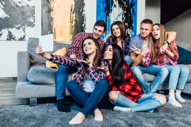 Gruppe lustiger junger Freunde, die zu Hause auf dem Sofa sitzen und zusammen Selfie machen..