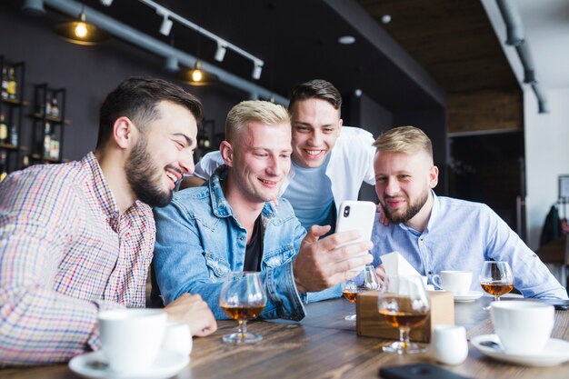 Gruppe männliche Freunde, die den Smartphone sitzt im Restaurant mit Getränken auf Tabelle betrachten