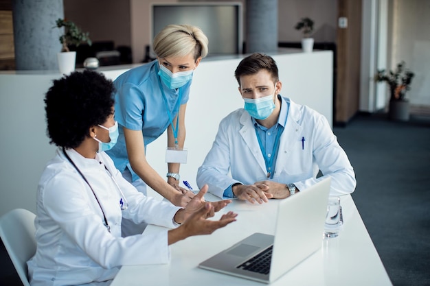 Gruppe medizinischer Experten, die sich während eines Meetings im Krankenhaus unterhalten, während sie einen Laptop verwenden