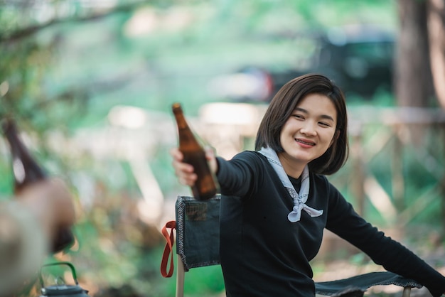 Gruppe schöner asiatischer Freundinnen, die sich vor dem Campingzelt entspannen. Sie genießen es, mit Spaß und Freude zusammen zu reden und Bier zu trinken