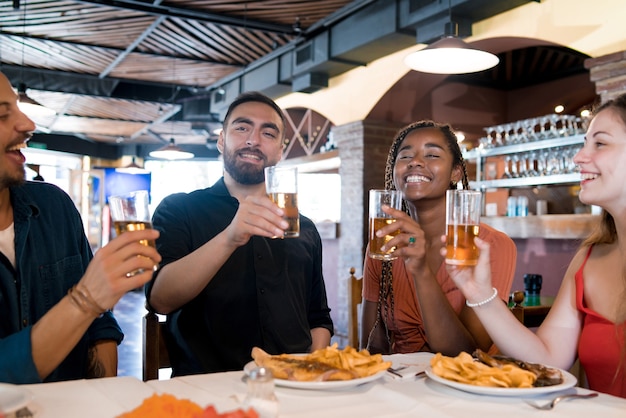 Gruppe verschiedener Freunde, die Bier trinken, während sie zusammen in einem Restaurant eine Mahlzeit genießen. Freunde-Konzept.