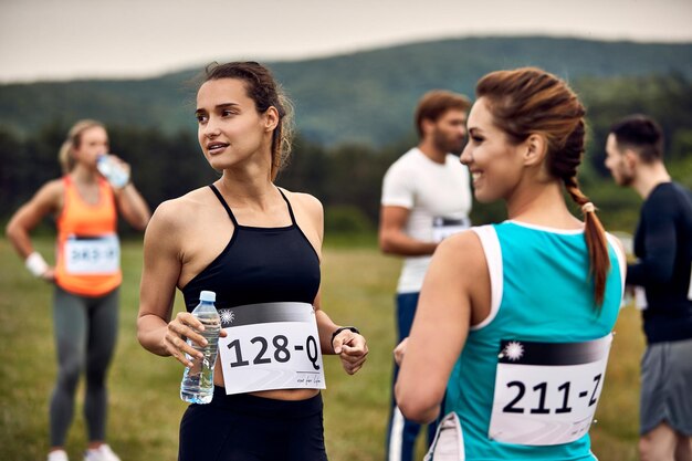 Gruppe von Athleten, die sich vor dem Marathonlauf in der Natur entspannen Der Fokus liegt auf der athletischen Frau, die eine Wasserflasche hält