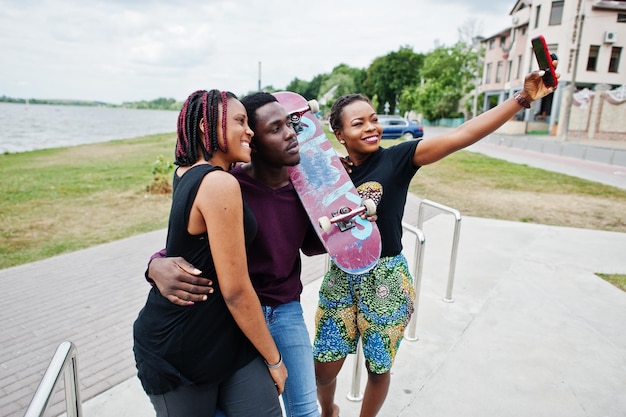 Gruppe von drei afroamerikanischen Freunden mit Skateboard, die am Telefon Selfie machen