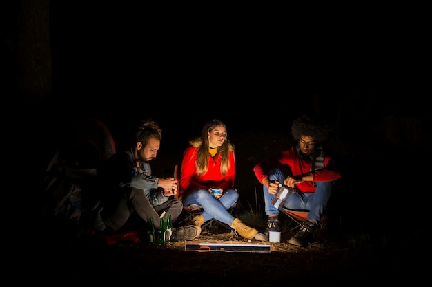 Gruppe von drei Freunden, die im Wald mit geführtem Licht nachts kampieren