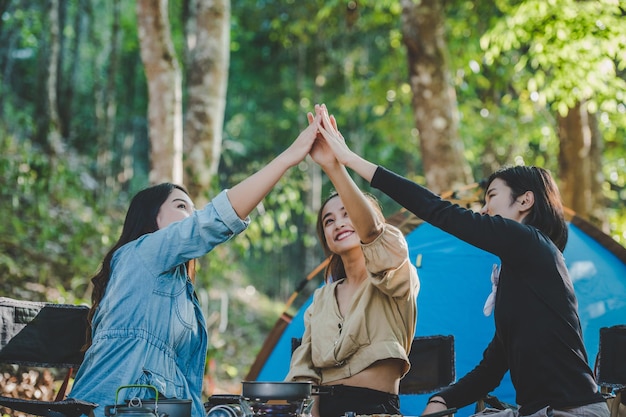 Gruppe von Frauen, die sich beim Camping mit einem zahnigen Lächeln und glücklich zusammen vor dem Campingzelt im Wald fünf geben