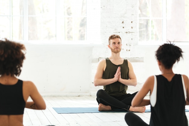 Gruppe von Frauen mit männlichem Lehrer, der auf Yogamatten sitzt