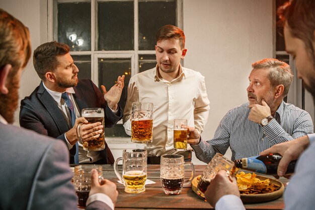 Gruppe von Freunden, die Abendgetränke mit Bier auf Holztisch genießen