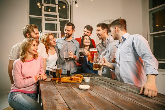 Gruppe von Freunden, die Abendgetränke mit Bier auf Holztisch genießen