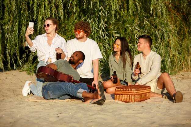 Gruppe von Freunden, die beim Picknick am Strand mit Biergläsern klirren