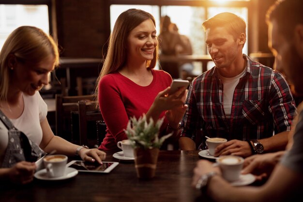 Gruppe von Freunden, die drahtlose Technologie verwenden, während sie sich in einem Café treffen Der Fokus liegt auf einem Paar, das gemeinsam ein Mobiltelefon verwendet