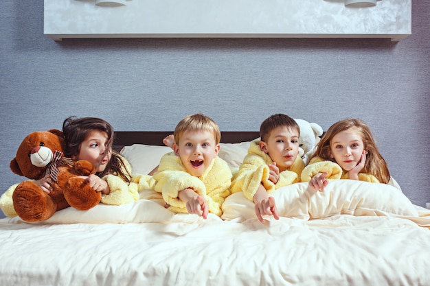 Gruppe von freunden, die gute zeit auf dem bett nehmen. glückliche lachende kinder, jungen und mädchen, die auf weißem bett im schlafzimmer spielen.