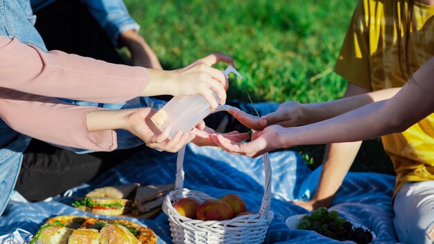 Gruppe von Freunden, die Hände bei einem Picknick mit Leckereien desinfizieren