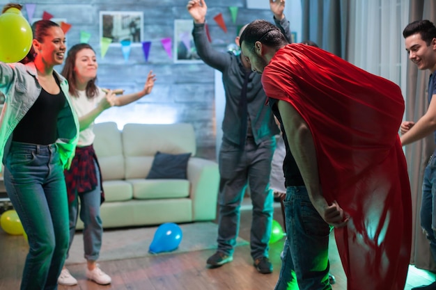 Gruppe von Freunden, die Männer mit Superhelden-Umhang auf der Party anfeuern.