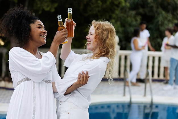 Gruppe von Freunden, die sich während einer weißen Party mit Getränken am Pool amüsieren