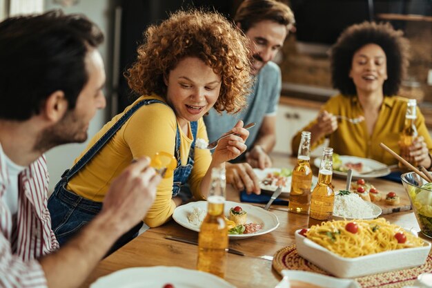 Gruppe von Freunden, die zusammen am Esstisch zu Mittag essen Der Fokus liegt auf der rothaarigen Frau