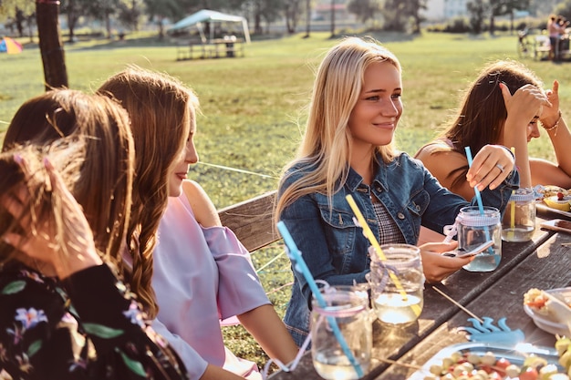 Gruppe von Freundinnen, die zusammen am Tisch sitzen und einen Geburtstag im Outdoor-Park feiern.