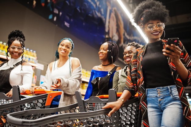 Gruppe von fünf afrikanischen Frauen, die mit Einkaufswagen im Supermarkt spazieren