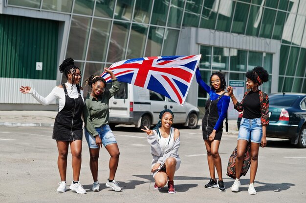 Gruppe von fünf afroamerikanischen Frauen, die zusammen auf dem Parkplatz mit britischer Flagge spazieren gehen