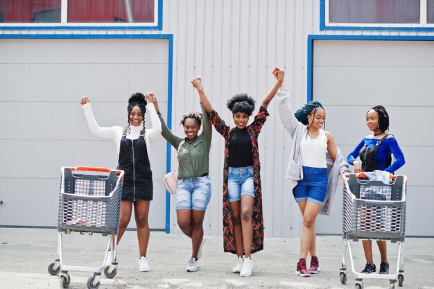 Gruppe von fünf afroamerikanischen Frauen mit Einkaufswagen, die gemeinsam Spaß im Freien haben